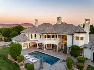 Back of house at dusk with a patio area, stucco siding, a chimney, a balcony, and a pool with connected hot tub