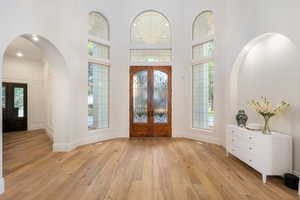 Foyer with french doors, arched walkways, light wood-style floors, a high ceiling, and healthy amount of natural light