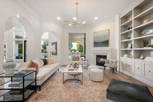 Living room featuring a glass covered fireplace, wood finished floors, crown molding, arched walkways, and a chandelier