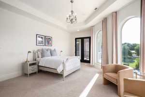 Bedroom with light carpet, french doors, a chandelier, access to outside, and a tray ceiling
