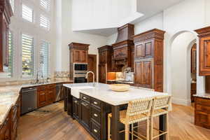 Kitchen with light stone countertops, a kitchen bar, a kitchen island with sink, light wood-style flooring, and a high ceiling