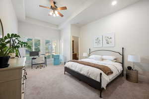 Bedroom featuring an office area, carpet, a tray ceiling, and a ceiling fan