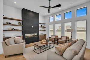 Living room featuring a tile fireplace, light wood-type flooring, recessed lighting, ceiling fan, and a towering ceiling