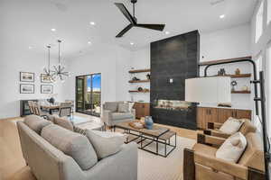 Living room featuring a fireplace, recessed lighting, ceiling fan, light wood-type flooring, and a high ceiling