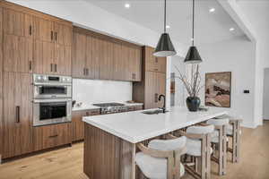 Kitchen featuring hanging light fixtures, light wood-style flooring, brown cabinetry, a breakfast bar area, and recessed lighting