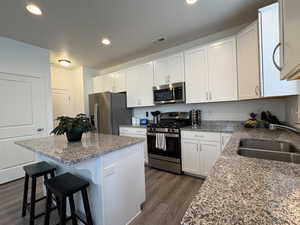 Kitchen with stainless steel appliances, dark wood finished floors, white cabinets, a center island, and a kitchen breakfast bar