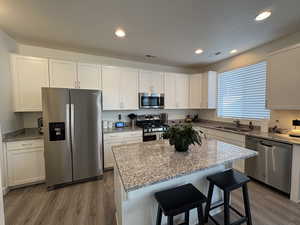 Kitchen featuring stainless steel appliances, white cabinets, light stone counters, dark wood-type flooring, and a breakfast bar