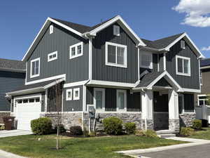 View of front of property featuring board and batten siding, a garage, stone siding, and roof with shingles