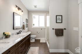 Bathroom with double vanity, a shower stall, and dark tile patterned flooring