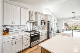 Kitchen with light countertops, stainless steel appliances, wall chimney range hood, white cabinets, and light wood-style floors