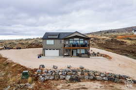 Rear view of property with dirt driveway, an attached garage, and a balcony