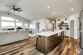 Kitchen with open floor plan, a kitchen breakfast bar, vaulted ceiling, a kitchen island with sink, and dark wood-type flooring