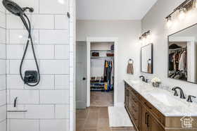 Full bath featuring double vanity, tiled shower, light tile patterned floors, and a walk in closet