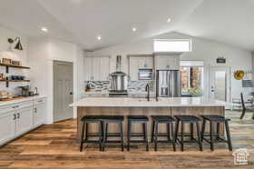 Kitchen featuring a breakfast bar, a large island with sink, stainless steel fridge, backsplash, and dark wood finished floors