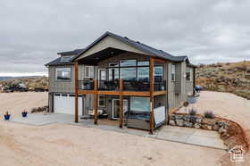Rear view of property with dirt driveway, an attached garage, a patio, and a deck