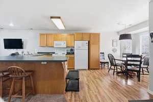 Kitchen featuring a breakfast bar, white appliances, dark countertops, light wood-type flooring, and a peninsula