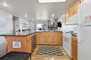 Kitchen with dark countertops, white appliances, light wood finished floors, and a peninsula
