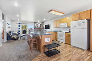 Kitchen with white appliances, a kitchen breakfast bar, open floor plan, dark countertops, and light brown cabinets