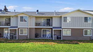 Rear view of house featuring a patio, board and batten siding, a balcony, roof with shingles, and a yard