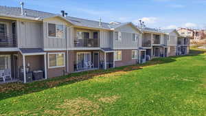 Back of property featuring board and batten siding, a balcony, a yard, a residential view, and a patio area