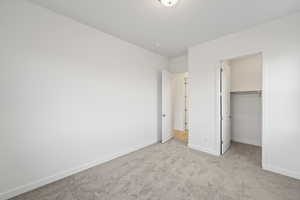 Unfurnished bedroom with a walk in closet and light colored carpet