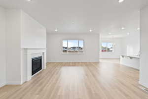 Unfurnished living room with recessed lighting, light wood-style flooring, a chandelier, and a glass covered fireplace