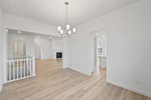 Unfurnished dining area featuring a fireplace, light wood-type flooring, and a chandelier