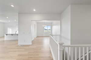 Corridor featuring a chandelier, light wood-style flooring, recessed lighting, and an upstairs landing