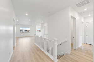 Hallway with an upstairs landing, recessed lighting, and light wood-style flooring