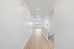 Hallway with an upstairs landing, light wood-style flooring, and recessed lighting