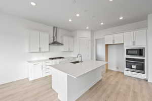 Kitchen featuring appliances with stainless steel finishes, recessed lighting, an island with sink, white cabinets, and light wood-type flooring