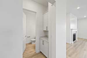 Bathroom featuring light wood-style flooring, a glass covered fireplace, recessed lighting, and vanity