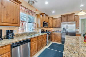 Kitchen with stainless steel appliances, light stone counters, light tile patterned floors, brown cabinets, and recessed lighting