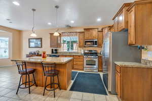 Kitchen featuring light stone counters, appliances with stainless steel finishes, brown cabinets, pendant lighting, and recessed lighting