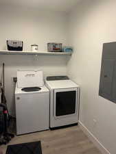 Laundry room with light wood-type flooring, electric panel, and washing machine and clothes dryer