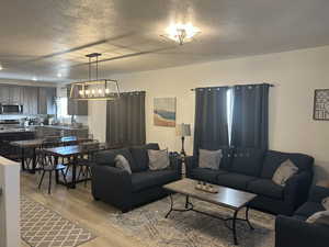 Living room with a textured ceiling, light wood-type flooring, and a chandelier
