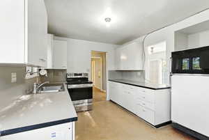 Kitchen featuring white cabinets, freestanding refrigerator, and stainless steel range with electric cooktop