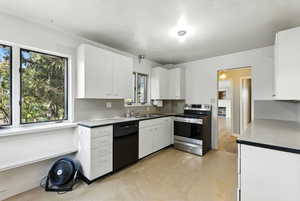 Kitchen featuring stainless steel electric stove, white cabinets, and black dishwasher