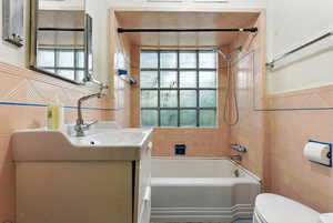Bathroom with tile walls, healthy amount of natural light, tub / shower combination, and vanity