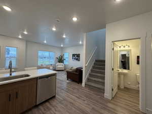 Kitchen featuring stainless steel dishwasher, open floor plan, dark wood-style flooring, recessed lighting, and light stone counters and view of half bath