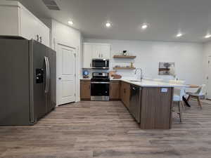 Kitchen featuring a peninsula, appliances with stainless steel finishes, open shelves, white cabinets, and light wood-style floors