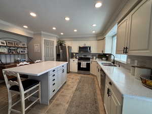 Kitchen with decorative backsplash, appliances with stainless steel finishes, recessed lighting, ornamental molding, and white cabinets