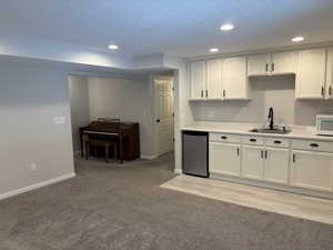 Kitchen with light countertops, recessed lighting, white cabinetry, light carpet, and white microwave