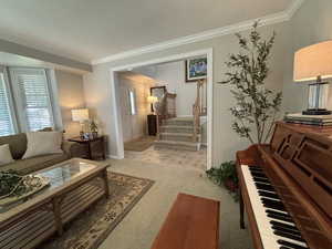 Living area with ornamental molding, light colored carpet, and stairway