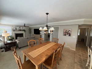 Tiled dining area with a tiled fireplace, a chandelier, crown molding, a textured ceiling, and carpet