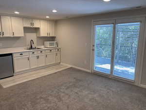 Kitchen with white cabinetry, light countertops, stainless steel dishwasher, light carpet, and recessed lighting