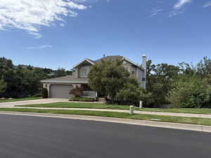 View of property hidden behind natural elements with a front yard, driveway, a chimney, and covered porch