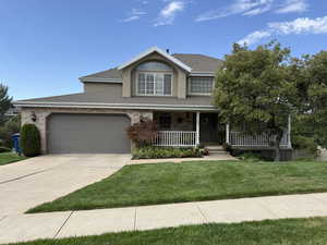 Traditional-style home with covered porch, a shingled roof, a front yard, and an attached garage