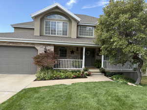 Traditional-style home with a porch, a shingled roof, a front lawn, concrete driveway, and an attached garage