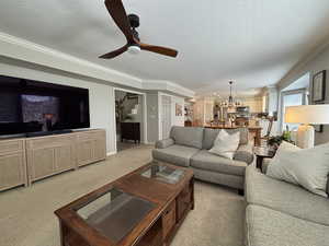 Living area with light carpet, a textured ceiling, crown molding, and a ceiling fan